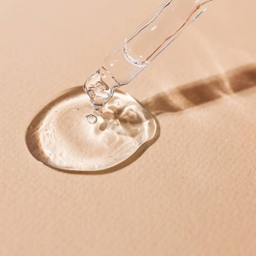 Transparent body serum flowing from a glass pipette front view.Cosmetic product close-up on a beige background.